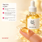 Fingertip holding a golden drop of Beauty of Joseon Glow Serum with the bottle behind it