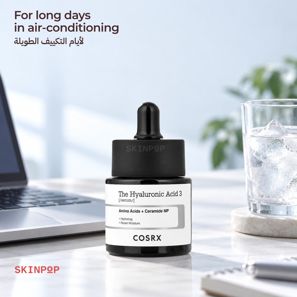 COSRX The Hyaluronic Acid 3 Serum on a desk next to a laptop and a glass of iced water