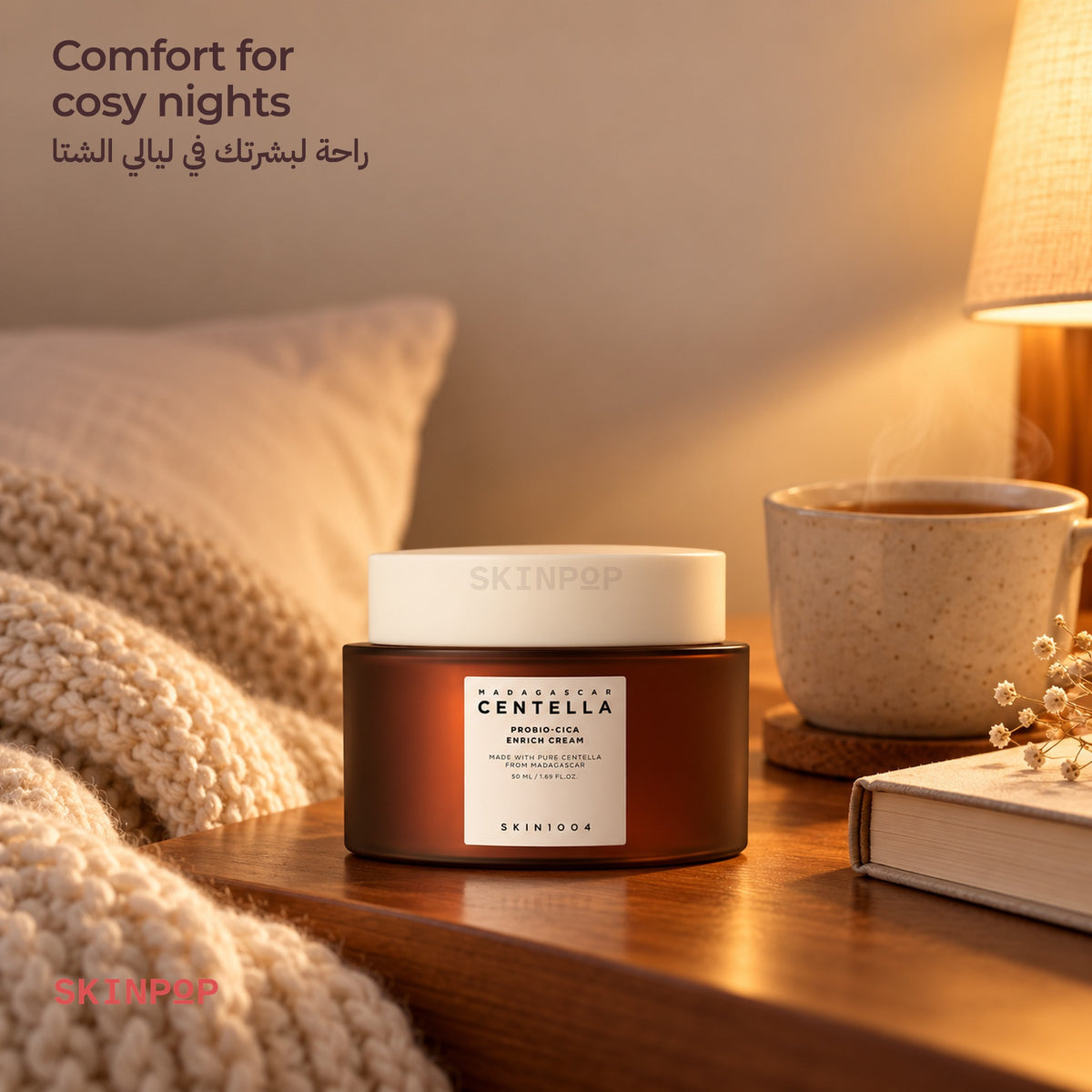 SKIN1004 Probio-Cica Enrich Cream on a bedside table with a knit blanket, a cup of tea and a book