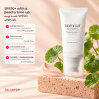 SKIN1004 Tone-Up Sunscreen tube on a peach stone block with fresh centella leaves