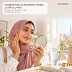 Woman holding a hand mirror and touching her cheek next to the SKIN1004 Tone-Up Sunscreen